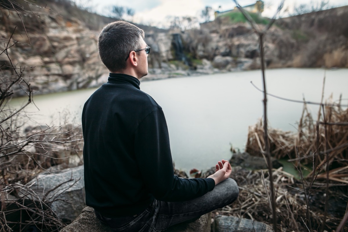 A man seen from behind, sitting alone at the edge of a lake