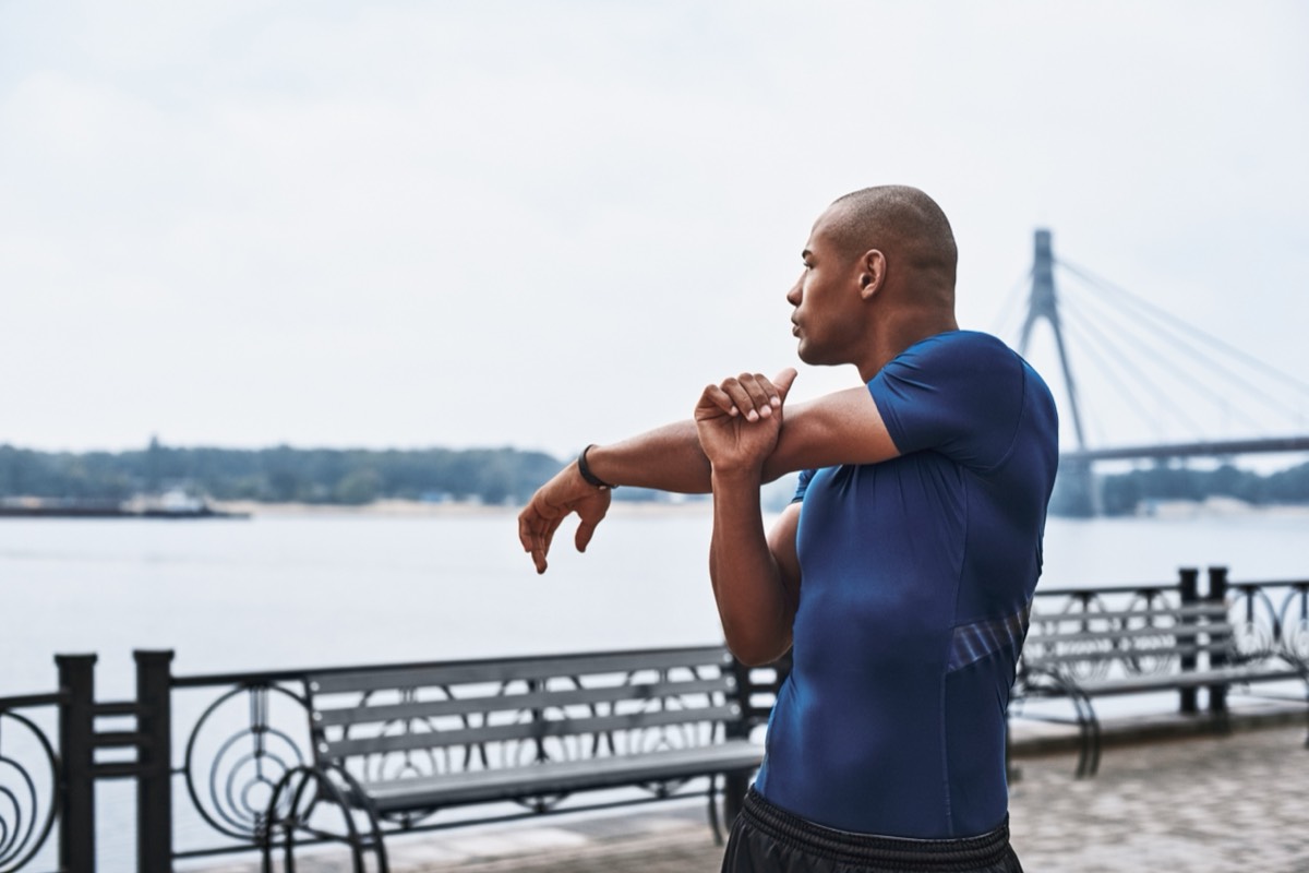 A man stretching his shoulder on a riverside promenade
