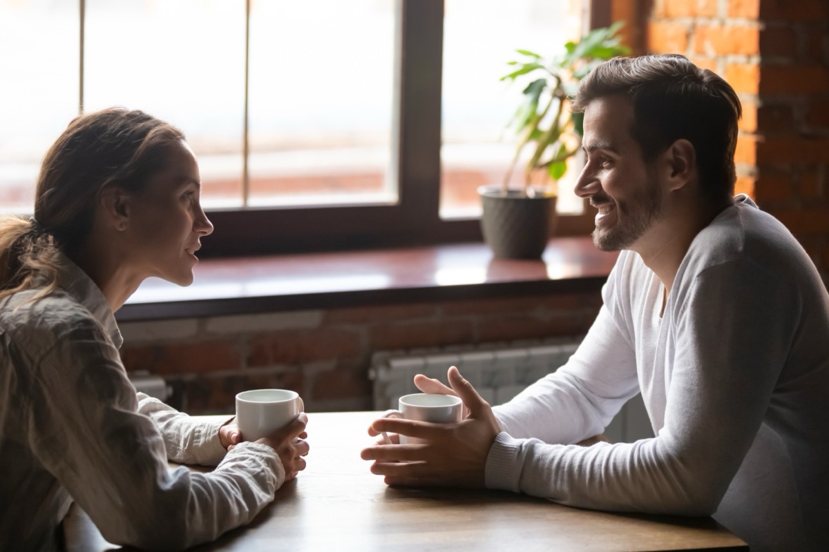 A man and woman talking over coffee at a café table by a window