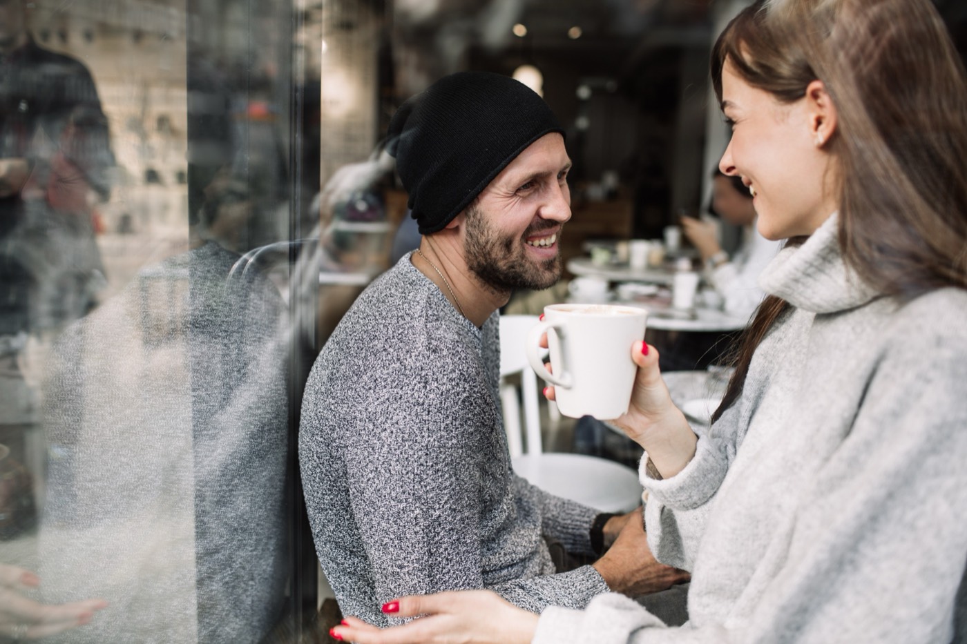 A man and woman laughing together outside a café, holding coffee