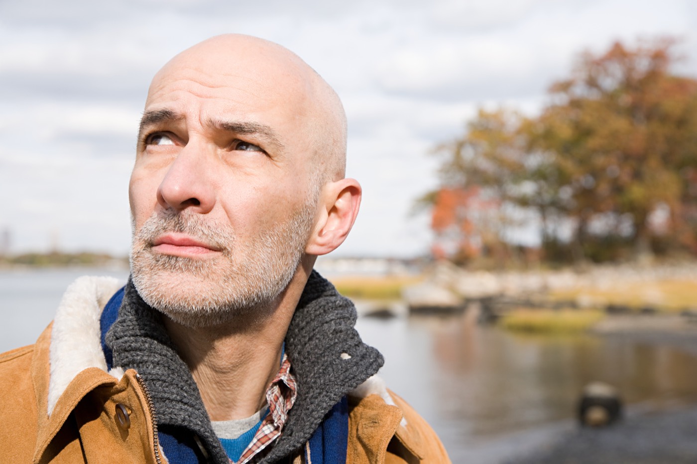 A man in his forties looking up in thought, standing by a river in autumn