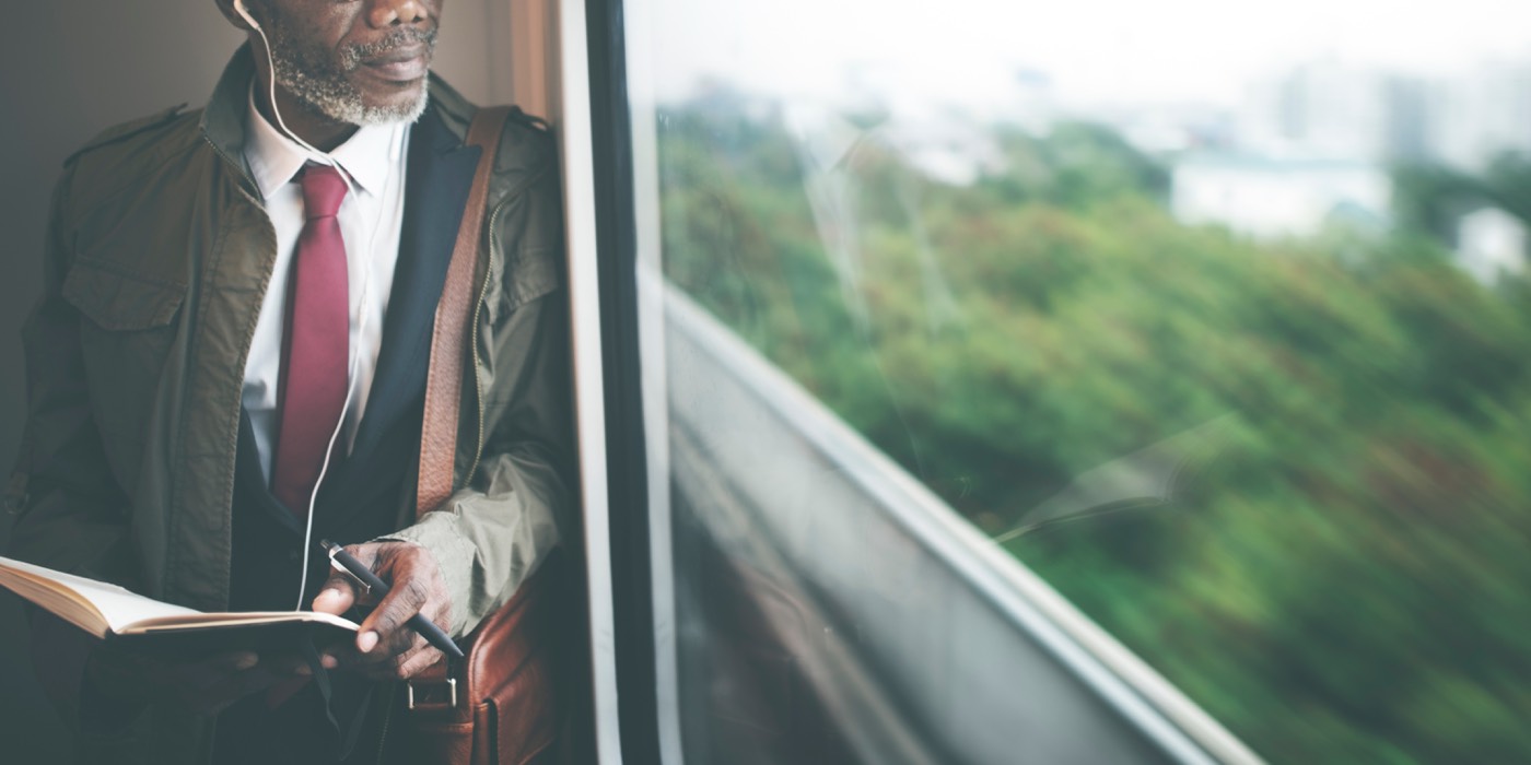 A man with a gray beard writing in a notebook on a moving train